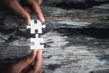Kadınların elinde yapboz parçaları var. Tahta arka planda yapboz parçasının beyaz detayları. Bir iş ekibi olarak birlikte çalışma kavramı. Olaya dahil olma fikri, başarı için çalışmak..