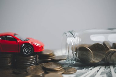 Araba sigortası işi, tasarruf satışı, yeni araba için vergi ve kredi. Arka planda bozuk para yığını olan oyuncak araba. Ulaşım finansmanını yönetmeyi planlıyorum. Araba için kredi