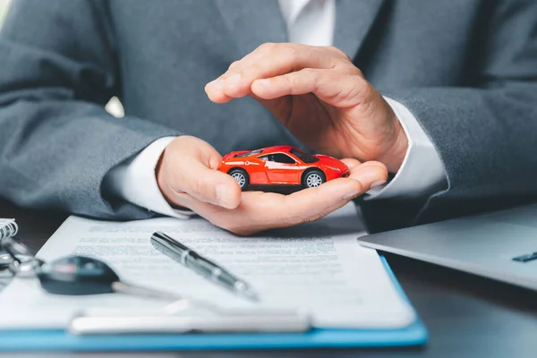Business woman\'s hand protecting red toy car on desk. Planning to manage transportation finance costs. Concept of car insurance business, saving buy - sale with tax and loan for new car.