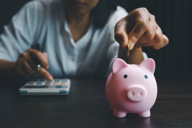 Business asian woman hand put coins in piggy bank on wood table background, saving money wealth and financial concept, finance, investment, Financial planning.Financial planning deposit for retirement