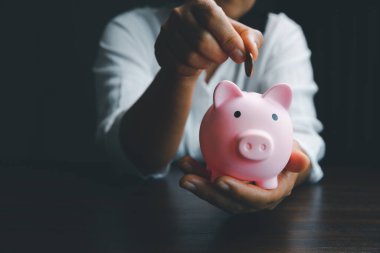 Business asian woman hand put coins in piggy bank on wood table background, saving money wealth and financial concept, finance, investment, Financial planning.Financial planning deposit for retirement