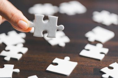 İş kadını, elinde bulmaca parçasıyla strateji ve çözüm önerisi tutuyor. Bir beyaz yapbozun yakın kısmı birbirine bağlanıyor. İşbirliğine katılma kavramı. Başarılı takım çalışması.