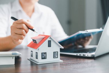 Emlakçılar konut satın almak ya da kiralamak için sözleşmeler teklif ediyorlar. İş adamı ev modeli ile el ele, küçük bina kırmızı evi. Konut kredisi sigortası eve taşınma ve emlak konsepti.