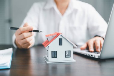 Emlakçılar konut satın almak ya da kiralamak için sözleşmeler teklif ediyorlar. İş adamı ev modeli ile el ele, küçük bina kırmızı evi. Konut kredisi sigortası eve taşınma ve emlak konsepti.