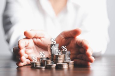 İş kadını eline oklu ve faiz oranı ve mortgage oranlarının yüzde sembolü olan bir tomar para veriyor. Simge yüzdesi sembolü ve yukarı bakan ok.
