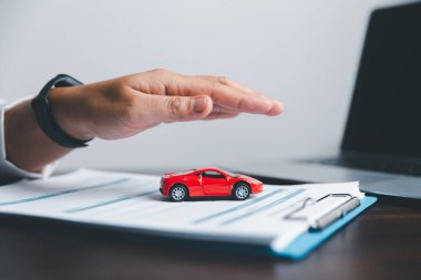 Masadaki kırmızı oyuncak arabayı koruyan iş kadını eli. Ulaşım finansmanını yönetmeyi planlıyorum. Araba sigortası işi kavramı, tasarruf satın alma - yeni araba için vergi ve kredi ile satış.