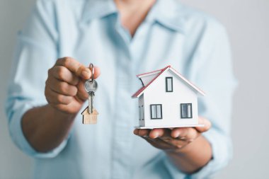 Kızın avucundaki kendi evinin anahtarı ve emlak kiralamak için bir ahşap. Evin modeli ve anahtarı evin kapısında. Emlakçı ev ve emlak sigortası teklif ediyor.