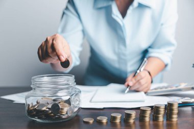 Business asian woman hand put coins in piggy bank on wood table background, saving money wealth and financial concept, finance, investment, Financial planning.Financial planning deposit for retirement