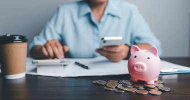 Business asian woman hand put coins in piggy bank on wood table background, saving money wealth and financial concept, finance, investment, Financial planning.Financial planning deposit for retirement