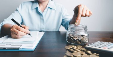 Business asian woman hand put coins in piggy bank on wood table background, saving money wealth and financial concept, finance, investment, Financial planning.Financial planning deposit for retirement