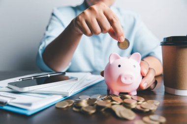 Business asian woman hand put coins in piggy bank on wood table background, saving money wealth and financial concept, finance, investment, Financial planning.Financial planning deposit for retirement