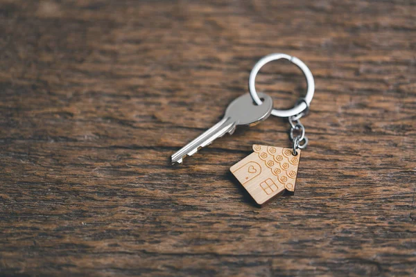 House key on a house shaped keychain resting on wooden floorboards concept for real estate renting property. House model and key in house door. Real estate agent offer house, property insurance.