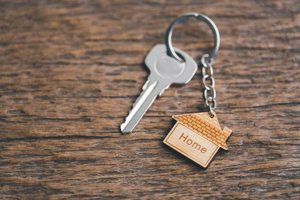 House key on a house shaped keychain resting on wooden floorboards concept for real estate renting property. House model and key in house door. Real estate agent offer house, property insurance.
