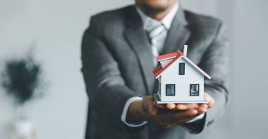 Emlak sigortası ve güvenlik kavramı. İnsanın jestini ve evin sembolünü koruyorum. Emlakçı kadına evin anahtarlarını veriyor ve müşteriden sözleşmeyi yasal hale getirmek için belgeleri imzalamasını istiyor..