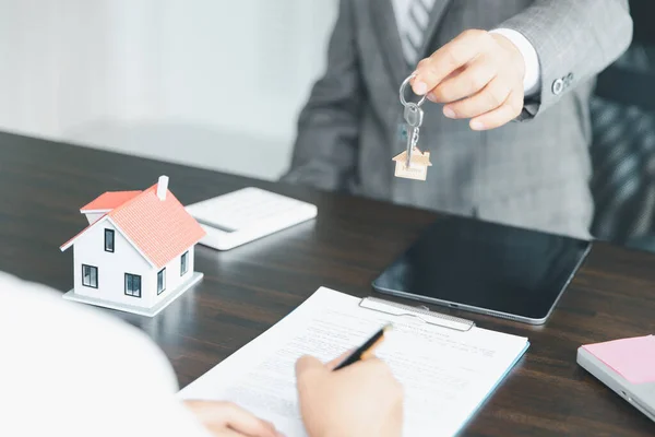 Home sales and home insurance concept. Estate agent giving house keys to woman and asked the customer to sign the documents to make the contract legally.