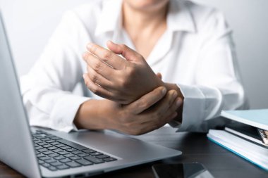 Bir ofis çalışanı dizüstü bilgisayarın önünde oturan Asyalı bir kadındır. Bir iş kadını ellerini ve parmaklarını strese sokuyor. Bir kadın ofis müdürü iş yerinde çok yoruldu..