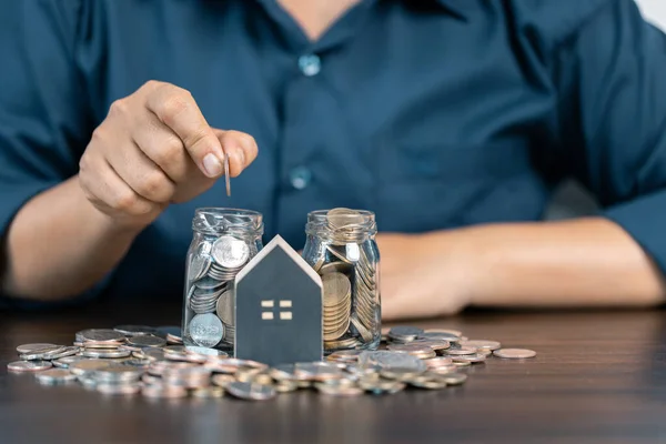 Saving money for house and real estate. Woman hand protecting on stack coins and house model on table.