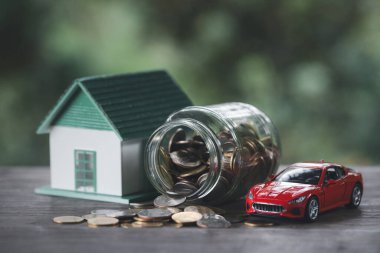 Altın sikkelerin üzerinde duran minyatür çift model ev ve araba ile doğal yeşil arka planda, gelecek ve emeklilik konseptine hazırlanmak için para biriktiriyor. Finans, yatırım ve gayrimenkul.