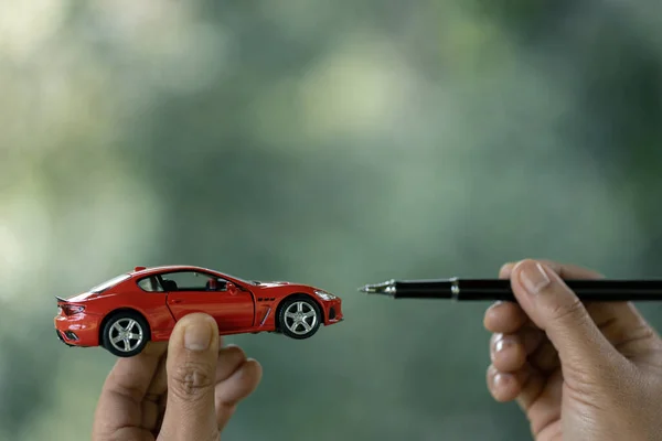 Saving money for car, Finance and car loan, Investment and business concept. Hand holding miniature car model and pen on nature green background.