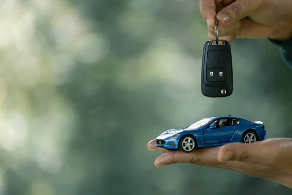 Saving money for car, Finance and car loan, Investment and business concept. Hand holding miniature car model and keys on nature green background.