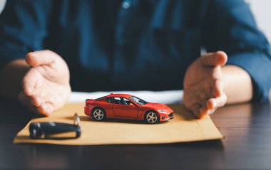 Business woman's hand protecting red toy car on desk. Planning to manage transportation finance costs. Concept of car insurance business, saving buy - sale with tax and loan for new car.