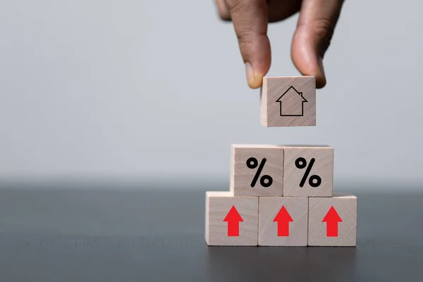 House and property investment and asset management concept. Interest rates, loan mortgage, house tax. Hand holding house icon on wooden block from stack with percent icon. Copy space for text.