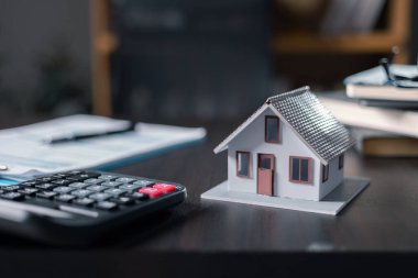 Model ev, evrak işleri ve nakit para: emlak, ev kredisi ve yatırım konsepti. Ev kredileri kavramı için ofis arka planında modern tasarım hesap makinesine ve kaleme sahip küçük evler