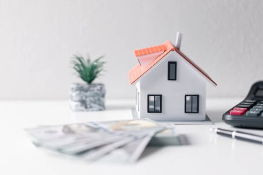 Paralı ev. Finans kavramı ya da gayrimenkul yeniden finanse etme. Evin sembolü dolarlarımızın arka planında duruyor. Emlak yatırımı. Ev kredisi oranı. Emeklilik için para biriktiriyorum.