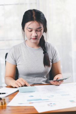 Genç Asyalı kadın yığınla para kazanıyor. Yatırım tasarruf konsepti, tasarruf, yatırım. Masada yığınla bozuk para ve banka hesap makinesi, tasarruf etmek için para ve gelir elde etmek için yatırım..