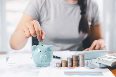 İş kadını domuz kumbarası ve masasında madeni paralar, finansal planlama ve yatırım konseptiyle para biriktiriyor. Genç Asyalı kadın yığınla para kazanıyor. Yatırım tasarruf, tasarruf, yatırım