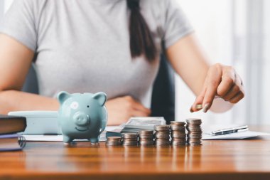 İş kadını domuz kumbarası ve masasında madeni paralar, finansal planlama ve yatırım konseptiyle para biriktiriyor. Genç Asyalı kadın yığınla para kazanıyor. Yatırım tasarruf, tasarruf, yatırım