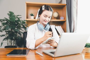 Asyalı kız öğrenci kulaklık takıyor internetten öğreniyor Webinar dersini izliyor bilgisayarlara bakıyor uzaktan ders alıyor notlar alıyor ya da evde sanal konferans öğretmeniyle görüşüyor..
