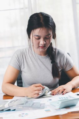 Genç Asyalı kadın yığınla para kazanıyor. Yatırım tasarruf konsepti, tasarruf, yatırım. Masada yığınla bozuk para ve banka hesap makinesi, tasarruf etmek için para ve gelir elde etmek için yatırım..
