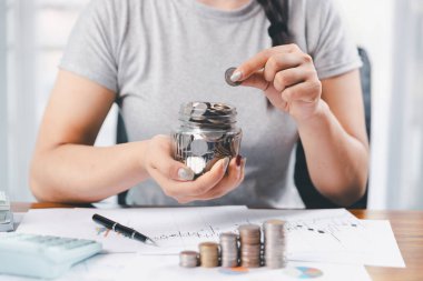 Genç Asyalı kadın yığınla para kazanıyor. Yatırım tasarruf konsepti, tasarruf, yatırım. Masada yığınla bozuk para ve banka hesap makinesi, tasarruf etmek için para ve gelir elde etmek için yatırım..