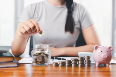 İş kadını domuz kumbarası ve masasında madeni paralar, finansal planlama ve yatırım konseptiyle para biriktiriyor. Genç Asyalı kadın yığınla para kazanıyor. Yatırım tasarruf, tasarruf, yatırım