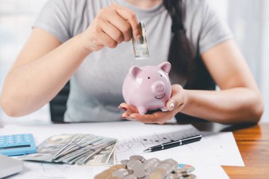 İş kadını domuz kumbarası ve masasında madeni paralar, finansal planlama ve yatırım konseptiyle para biriktiriyor. Genç Asyalı kadın yığınla para kazanıyor. Yatırım tasarruf, tasarruf, yatırım