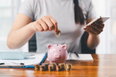 İş kadını domuz kumbarası ve masasında madeni paralar, finansal planlama ve yatırım konseptiyle para biriktiriyor. Genç Asyalı kadın yığınla para kazanıyor. Yatırım tasarruf, tasarruf, yatırım