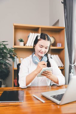 Asyalı kız öğrenci kulaklık takıyor internetten öğreniyor Webinar dersini izliyor bilgisayarlara bakıyor uzaktan ders alıyor notlar alıyor ya da evde sanal konferans öğretmeniyle görüşüyor..