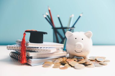 Eğitim için para biriktirme kavramı, öğrenci kredisi, gelecekte burs. Mezuniyet şapkalı domuz kumbarası, bir yığın bozuk para. Mezuniyet şapkalı dünya küresi, masada dolar banknotları. Okul harcı