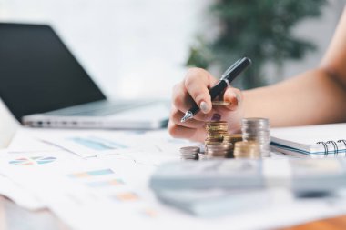 Genç Asyalı kadın yığınla para kazanıyor. Yatırım tasarruf konsepti, tasarruf, yatırım. Masada yığınla bozuk para ve banka hesap makinesi, tasarruf etmek için para ve gelir elde etmek için yatırım..