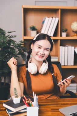 Asyalı kız ev ödevi yapıyor ve evde çalışıyor. Masa başında dizüstü bilgisayar kullanan bir kadın webinar izleyen, online çalışan, internet dersine giren ya da evden kumandalı sanal telefon görüşmesi yapan notlar yazıyor..