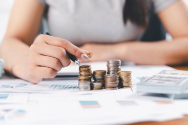 Genç Asyalı kadın yığınla para kazanıyor. Yatırım tasarruf konsepti, tasarruf, yatırım. Masada yığınla bozuk para ve banka hesap makinesi, tasarruf etmek için para ve gelir elde etmek için yatırım..