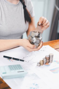 Genç Asyalı kadın yığınla para kazanıyor. Yatırım tasarruf konsepti, tasarruf, yatırım. Masada yığınla bozuk para ve banka hesap makinesi, tasarruf etmek için para ve gelir elde etmek için yatırım..