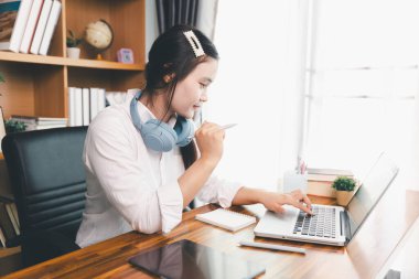 Asyalı kız öğrenci kulaklık takıyor internetten öğreniyor Webinar dersini izliyor bilgisayarlara bakıyor uzaktan ders alıyor notlar alıyor ya da evde sanal konferans öğretmeniyle görüşüyor..