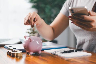 İş kadını domuz kumbarası ve masasında madeni paralar, finansal planlama ve yatırım konseptiyle para biriktiriyor. Genç Asyalı kadın yığınla para kazanıyor. Yatırım tasarruf, tasarruf, yatırım