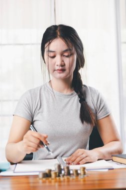 Genç Asyalı kadın yığınla para kazanıyor. Yatırım tasarruf konsepti, tasarruf, yatırım. Masada yığınla bozuk para ve banka hesap makinesi, tasarruf etmek için para ve gelir elde etmek için yatırım..