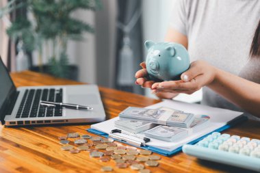 İş kadını domuz kumbarası ve masasında madeni paralar, finansal planlama ve yatırım konseptiyle para biriktiriyor. Genç Asyalı kadın yığınla para kazanıyor. Yatırım tasarruf, tasarruf, yatırım