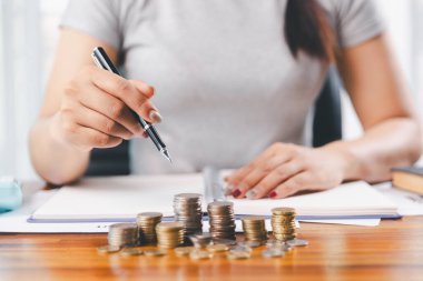 Genç Asyalı kadın yığınla para kazanıyor. Yatırım tasarruf konsepti, tasarruf, yatırım. Masada yığınla bozuk para ve banka hesap makinesi, tasarruf etmek için para ve gelir elde etmek için yatırım..