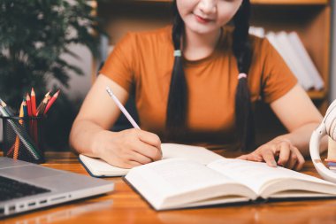 Asyalı kız ev ödevi yapıyor ve evde çalışıyor. Masa başında dizüstü bilgisayar kullanan bir kadın webinar izleyen, online çalışan, internet dersine giren ya da evden kumandalı sanal telefon görüşmesi yapan notlar yazıyor..