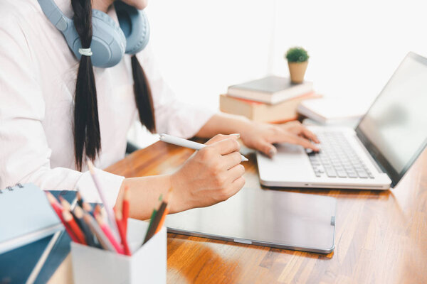 Asian girl student wear headphones learning online watching webinar class looking at laptop computer elearning remote lesson making notes or video calling virtual conference meeting teacher at home.